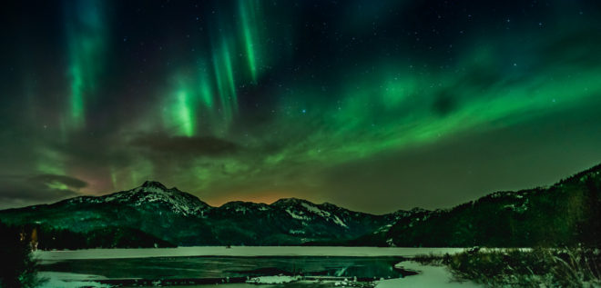 Green Northern Lights shimmering over water with mountains in the background